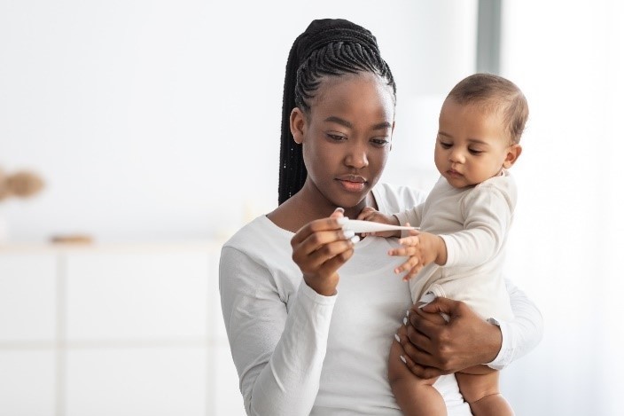 image shows a woman holding a baby and looking at a thermometer