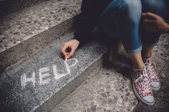 photo of a sidewalk w/legs of a person sitting on a step and chalk writing the word HELP