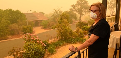 photo of a woman standing on her balcony, wearing a mask, looking out at a very smokey neighborhood