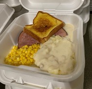 a sandwich, corn, and other food in a styrofoam container