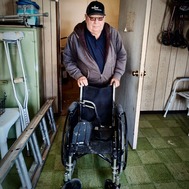 Bill Beasley stands behind a child sized wheelchair