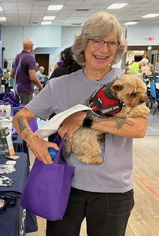 smiling woman holding small service dog at community center