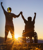 person standing holding hands with person in wheelchair, facing sun