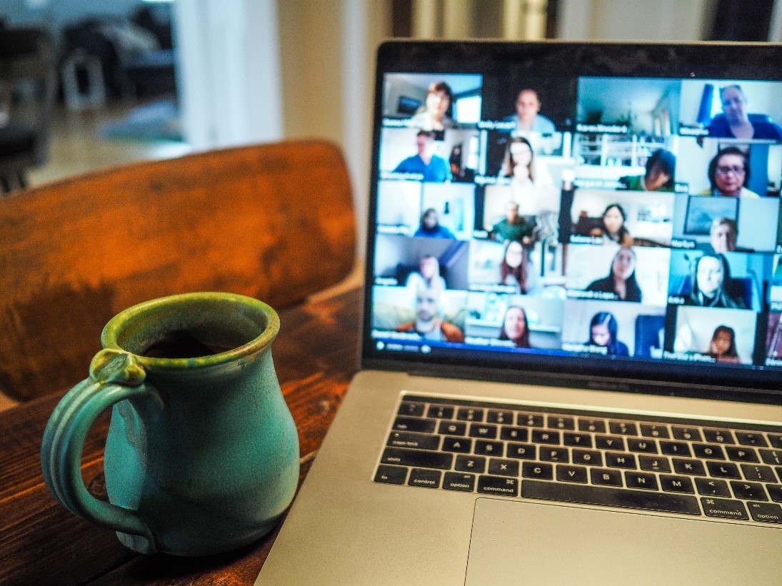 Laptop showing participants in a virtual meeting next to coffee mug