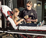 EMT assisting child on a gurney with a pediatric restraint system and teddy bear