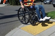 A  person crosses the street in a wheelchair using an ADA accessible ramp.