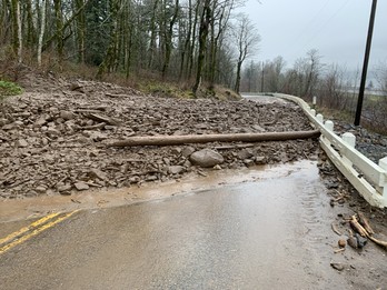 A large pile of rocks, mud and trees cover the entire highway. 