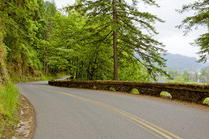 A winding road with an arched rock railing, surrounded by greenery and overlooking a blue sky. 