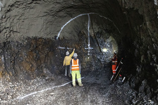 Three workers stand in a rock tunnel with a circular outline on the back wall. 
