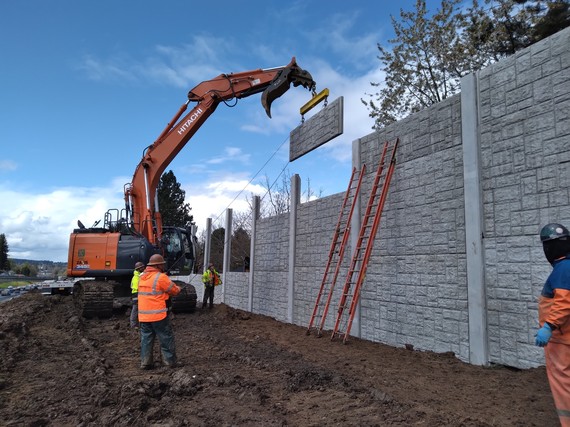 Crews use a crane to lift a panel for a sound wall.