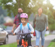 Girl on bicycle with family on paved bike path.