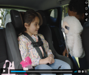 Child in car seat while adult hands them a sloth stuffed animal.