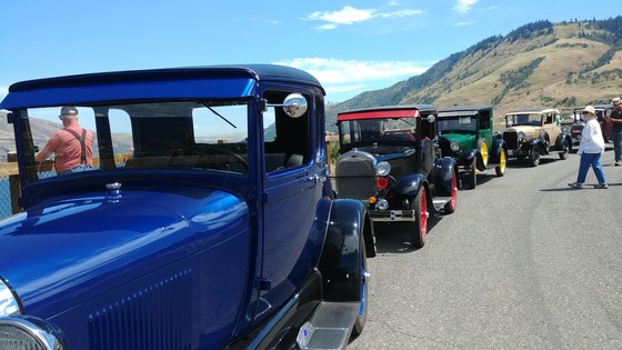 A line of five antique cars ranging from blue, black, green, tan and red. 