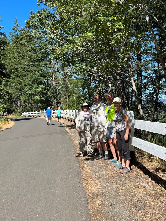 Four people stand next to each other smiling at the camera with a white wood railing behind them along a trail