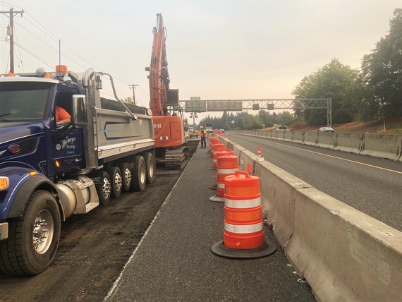 A dump truck and excavator on the side of OR 217 behind a concrete barrier.