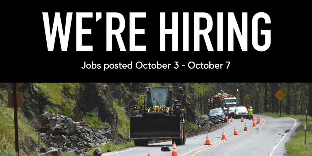 Tractor on a road with orange cones near grassy rock wall.