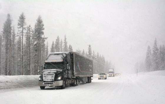 Semi-truck and other vehicles drive on snow-covered Highway 138E