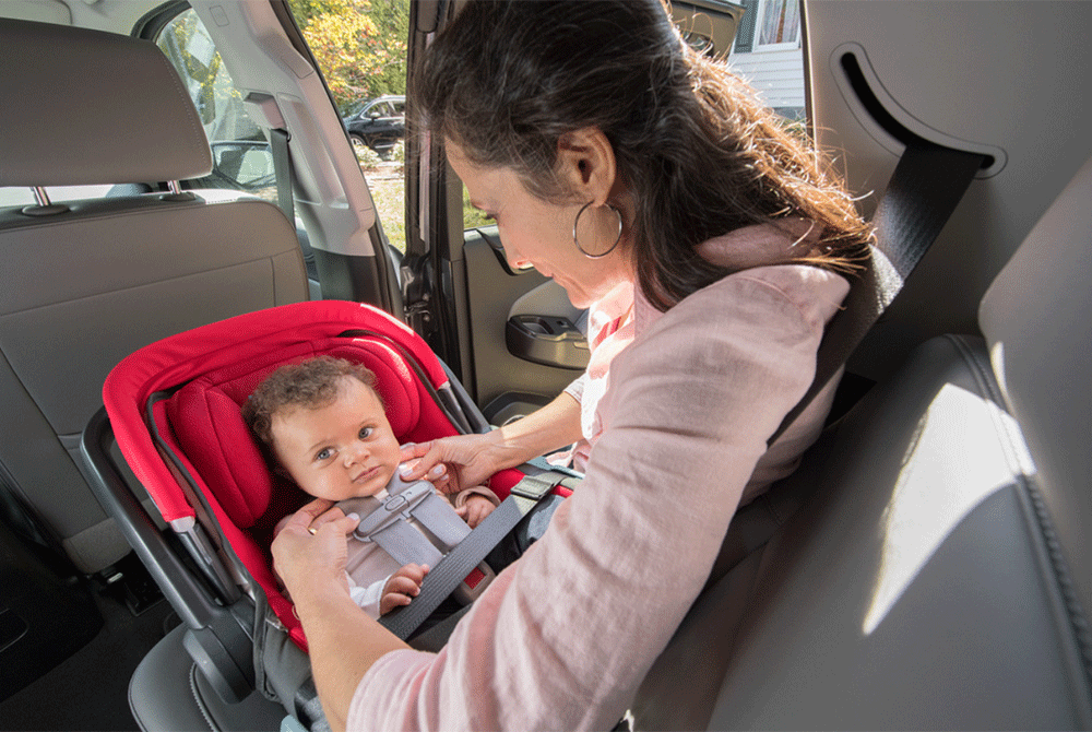 Mother buckling in an infant in a rear facing child car seat