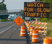 Orange traffic cones and barrels line the side of a highway. VMS board "WATCH FOR SLOW TRAFFIC."