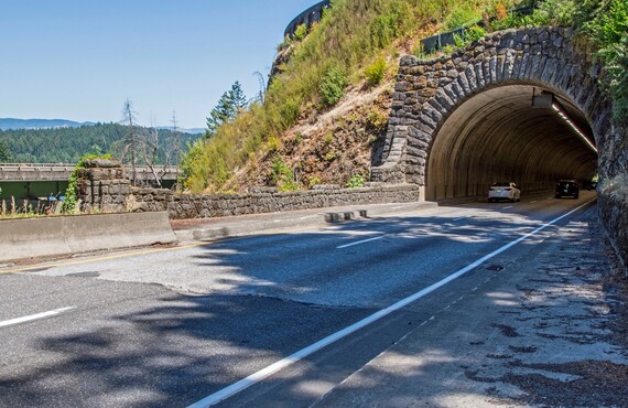 The stone masonry face of the tunnel is in the background. Deep ruts are visible on the two highway lanes. 