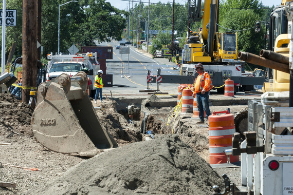 In the background is the highway. In the foreground is piles of dirt, holes, and heavy equipment. 