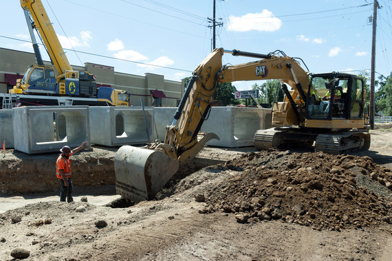 In the background are large concrete boxes. Heavy equipment excavated a hole. 