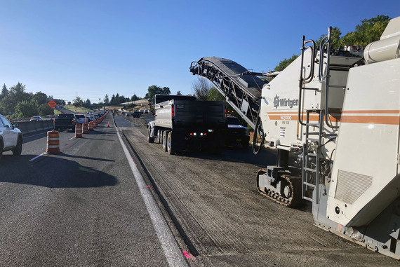 One lane of traffic on the left. Next to the closed lane, crews rebuild the base to support the pavement of the new auxiliary lane. 