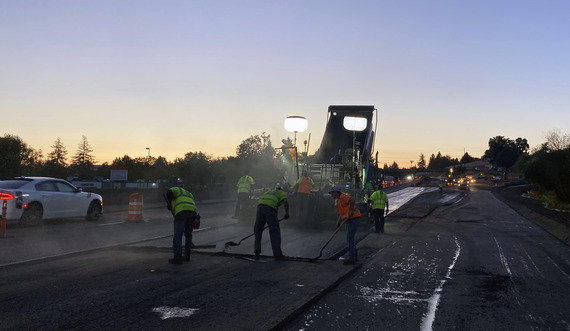 At night, crews work behind the asphalt truck laying down fresh pavement for the future auxiliary lane. 
