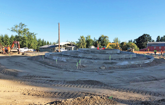 Circular raised concrete curbs in the intersection, forming the beginning of a roundabout. Dirt surrounds it. 