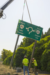Two ODOT construction workers standing up a new sign indicating the new roundabout