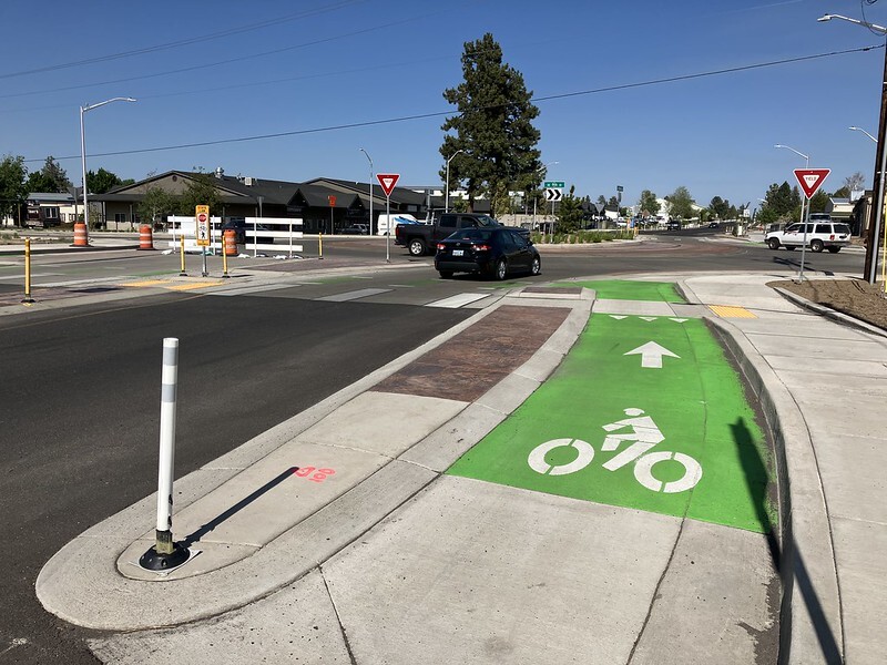 A painted green bike lane merges with a travel lane at a roundabout
