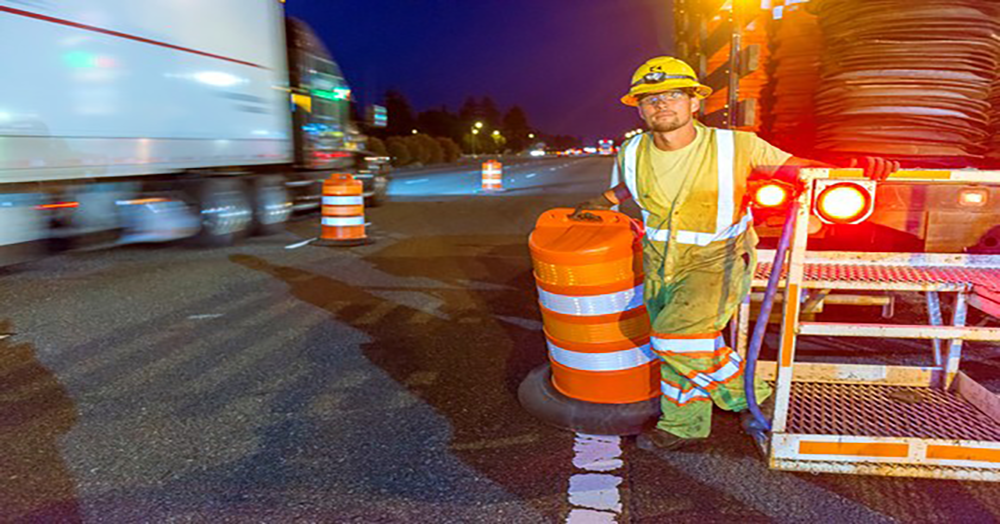 Construction worker next to orange barrel standing near traffic