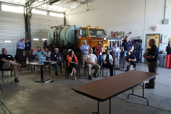 Legislators listen to a presentation in an Albany maintenance facility garage with equipment in the background