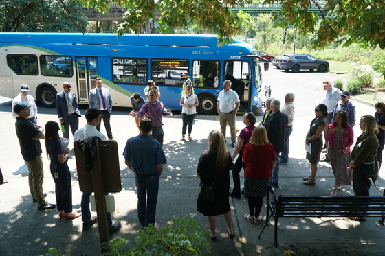 Lawmakers and agency leaders listen to presentation near Eugene-Springfield bridge with Lane Transit District bus in the background