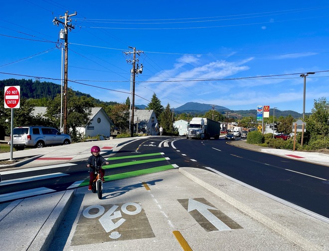 A child rides a bike in a new bike lane in Philomath with a semi-truck approaching in the background. 