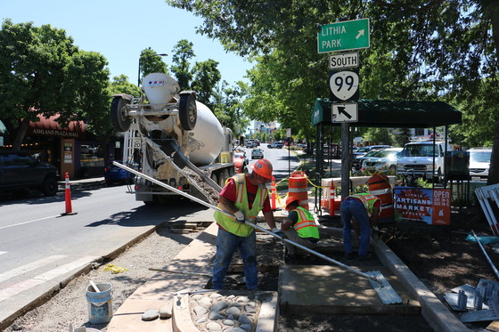 A dump truck pours concrete next to workers to create a base for a new sidewalk in Ashland.