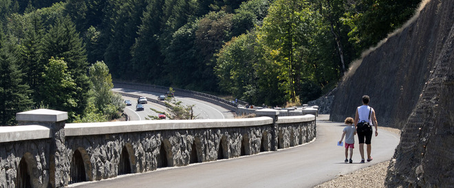 An adult and young child walk along a pedestrian path holding hands