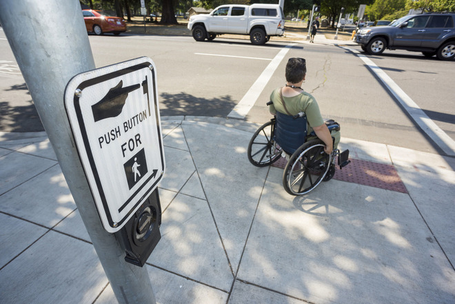 A person in a wheelchair waits at a street corner for a safe time to cross the street.