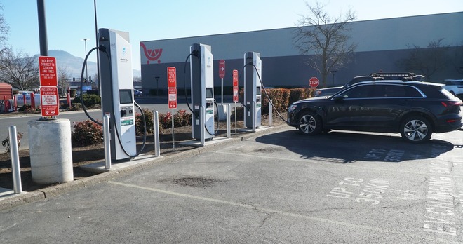 A row of DV fast chargers in a Fred Meyer parking lot with a black EV charging up at the far station.