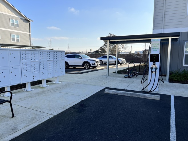 An EV charging station at the head of an open parking spot in an apartment complex on a sunny morning.