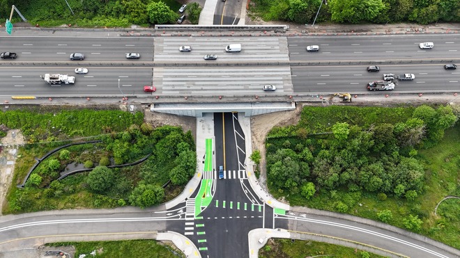 Aerial view of traffic on an interstate road over a local one with bike and pedestrian crossings marked in green.