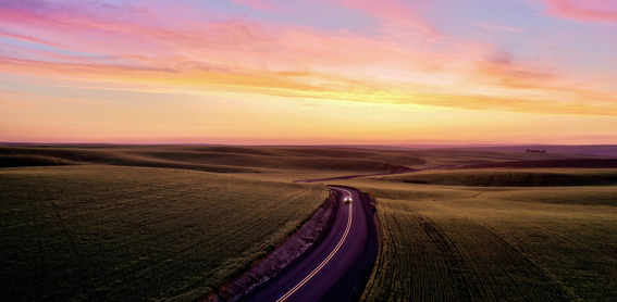 aerial view of a truck driving on a two-lane highway in the middle of farmland