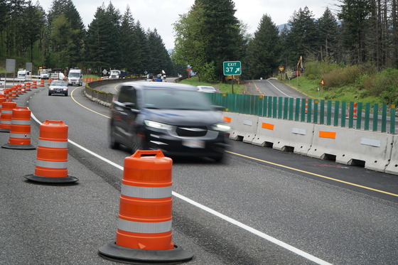 Car drive through a single lane work zone lined by orange barrels.