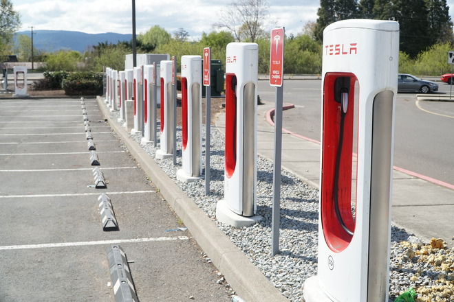 A row of white and red Tesla fast chargers in a parking lot.