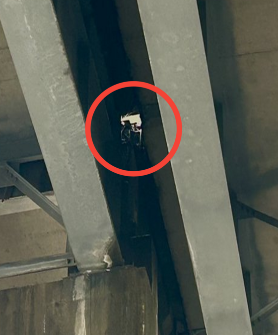 Underside of I-5 bridge between two supporting steel beams, a hole formed allowing viewers to see through the bridge