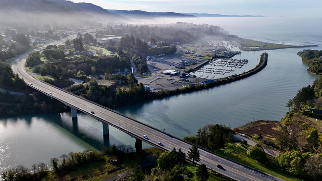 Aerial view of a bridge over a river that empties into the ocean of a foggy morning.