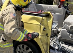 Vehicle Extrication being performed on a yellow van by a firefighter with a saw