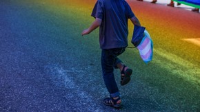 Running child with transgender flag in hand, on a rainbow colored street