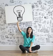 person sitting on the ground, raising hand above a mural with a lightbulb icon
