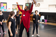 drama teacher in red outfit with arms raised with students